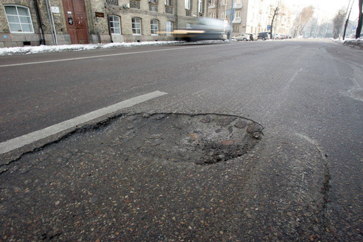 Atvirose vietose asfaltuotos kelių dangos yra šlapios. Tirpstant ledui veriasi duobės.