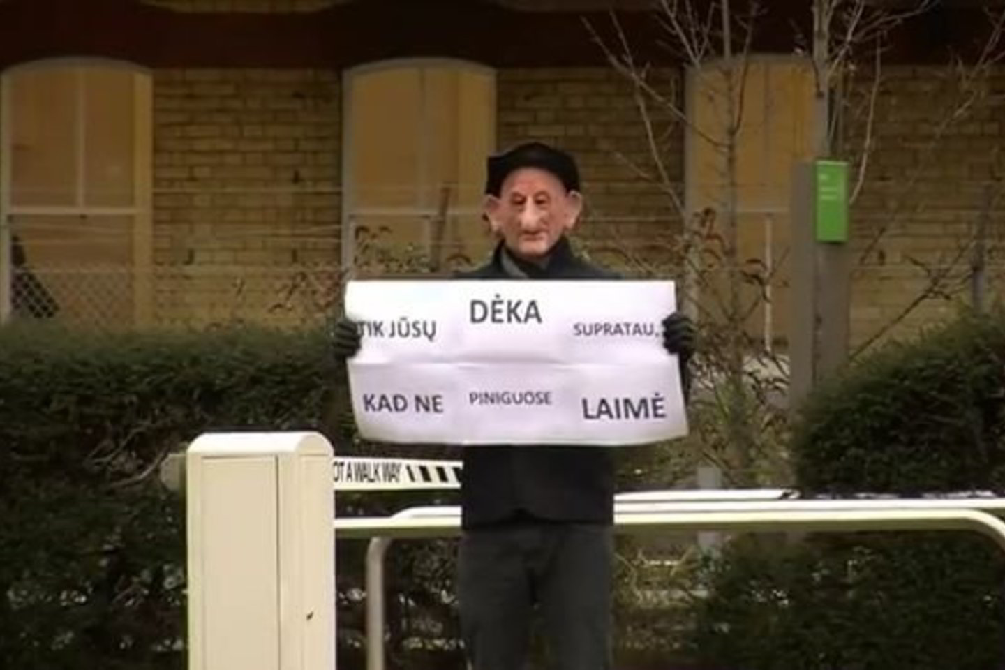 Kauke veidą slepiantis „pensininkas“ rankose jis laiko plakatą „Tik jūsų dėka supratau, kad ne piniguose laimė“.