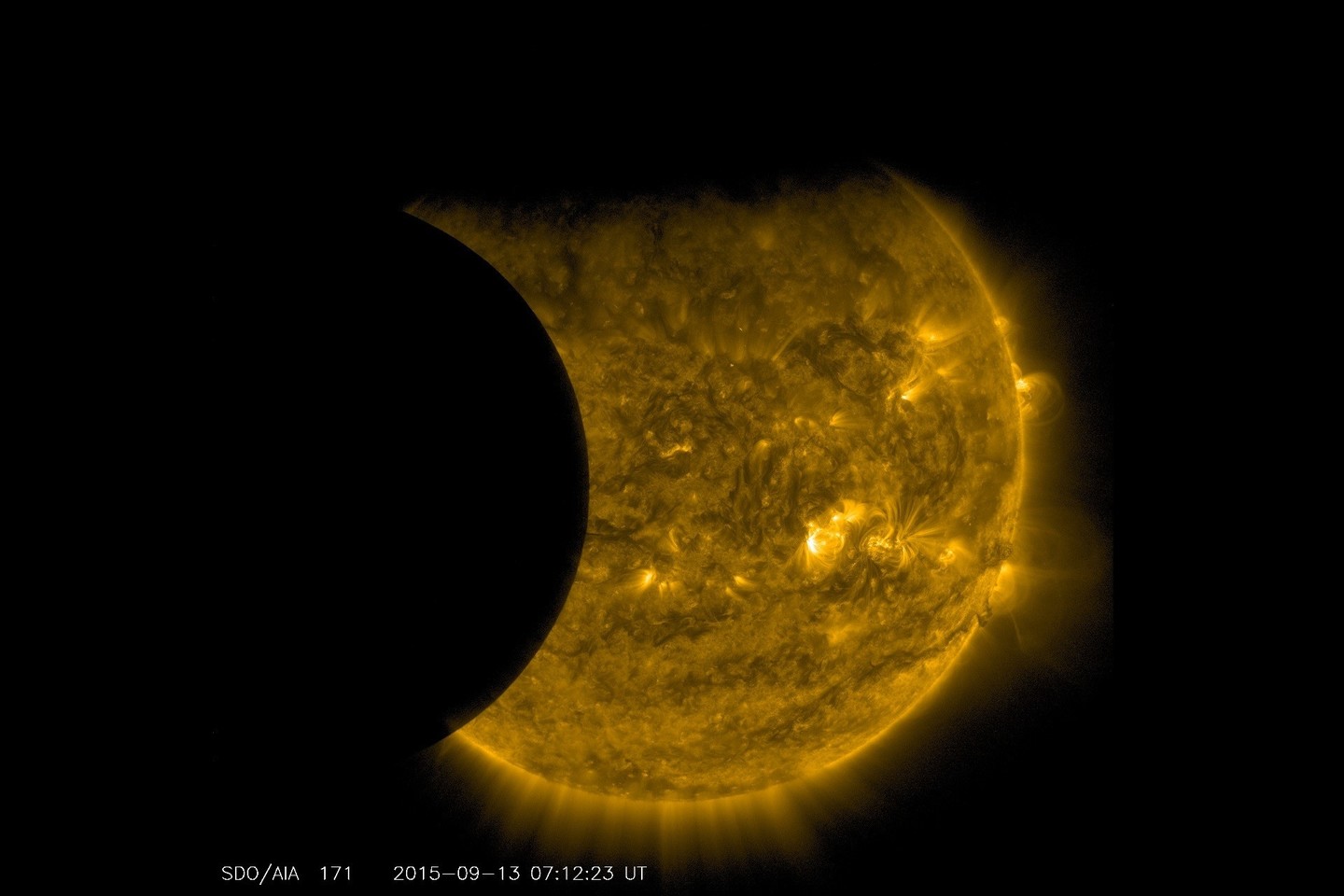 Nuotraukoje Žemė „atkando“ viršutinės disko dalies – kadangi planeta turi atmosferą, vaizdas yra blyškus. Atmosferos neturinčio Mėnulio kontūras yra ryškus, jis užstoja kairįjį Saulės disko pakraštį.<br>NASA/SDO nuotr.