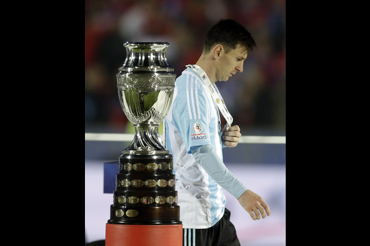 Argentinos rinktinės žvaigždė Lionelis Messi eina pro „Copa America“ trofėjų, delne gniauždamas turnyro sidabrą.<br>AP nuotr.
