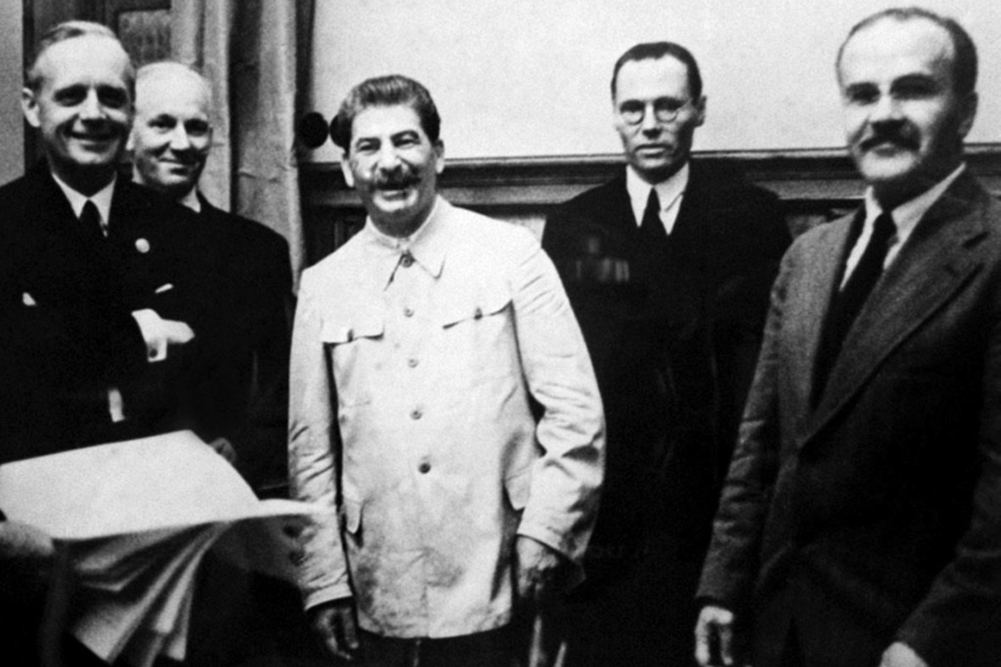 Džiaugsmas pasirašius Molotovo–Ribentropo paktą. Pirmoje eilėje iš kairės – J. fon Ribentropas, J. Stalinas ir V. Molotovas.<br> Knygos iliustracija.