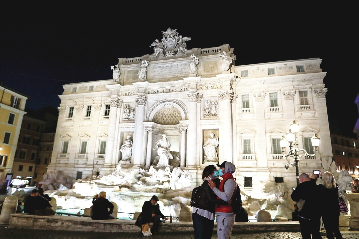 Prie ištuštėjusio Trevio fontano žmonės laikosi saugaus atstumo, o poros bučiuojasi tik su apsauginėmis kaukėmis.<br>„Reuters“/„Scanpix“ nuotr.