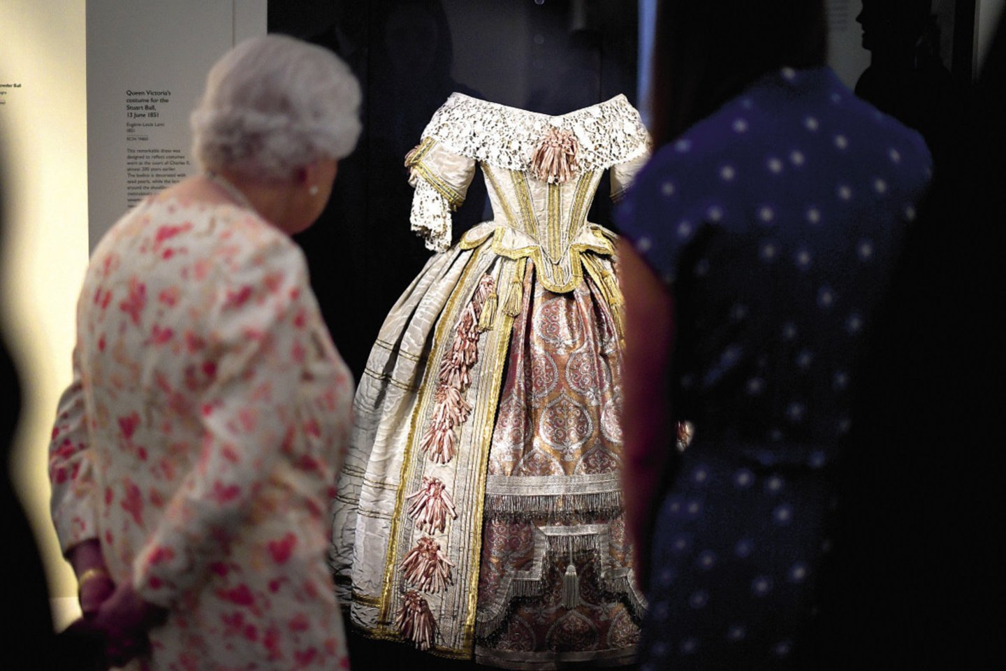 Elizabeth II apžiūri Viktorijos dėvėtą suknelę.<br> Scanpix nuotr.