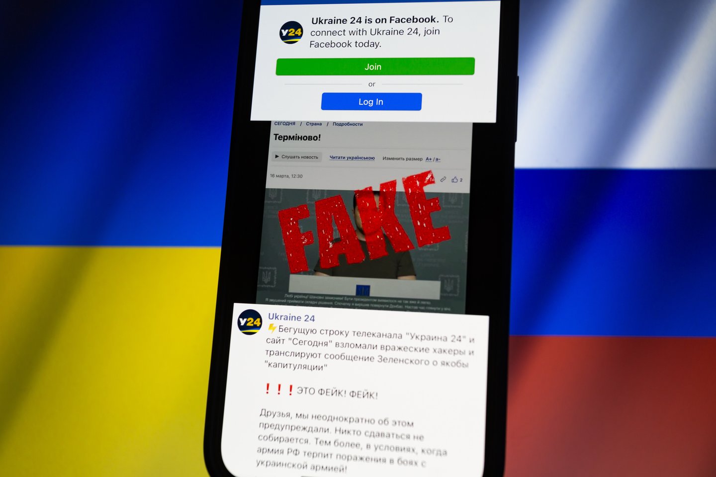 „Facebook“ puslapis rodomas išmaniojo telefono fone, kurio fone matyti apkarpytos plevėsuojančios Ukrainos ir Rusijos vėliavos.<br> Zuma Press/Scanpix nuotr.