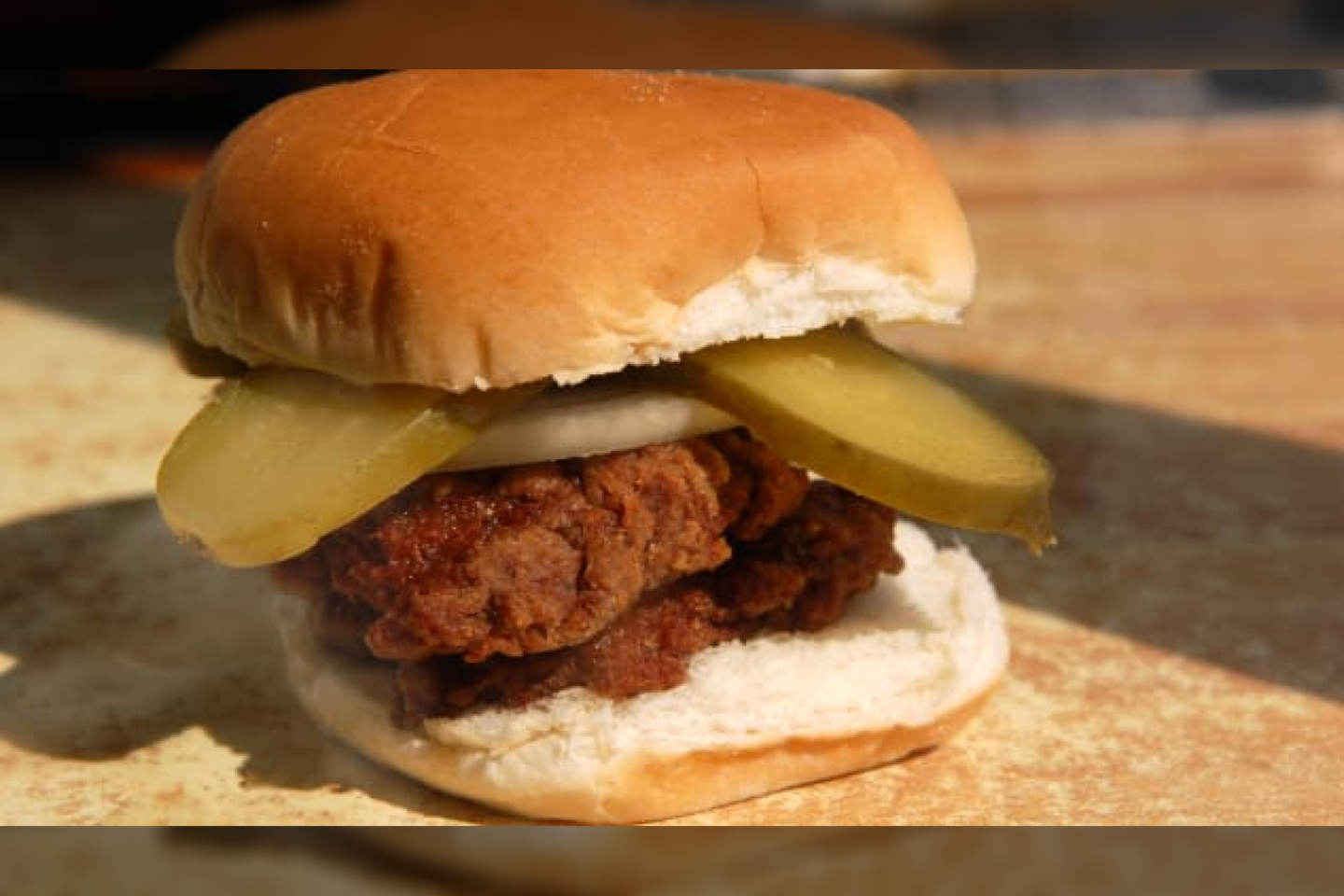  „Hamburger Wagon“ mėsainis patiekiamas su marinuotais agurkais, svogūnais, druska ir pipirais.<br> „Hamburger America“ nuotr.