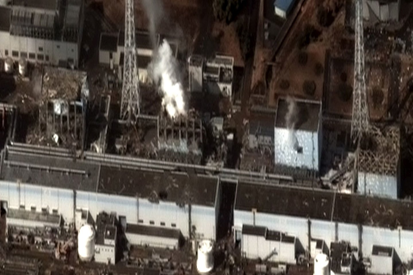 2011 m. kovo 16 d., keturi pažeisti reaktorių pastatai (iš kairės: 4, 3, 2 ir 1 blokai). Vandenilio ir oro sprogimai 1, 3 ir 4 blokuose padarė žalos konstrukcijoms.<br> Wikimedia commons.