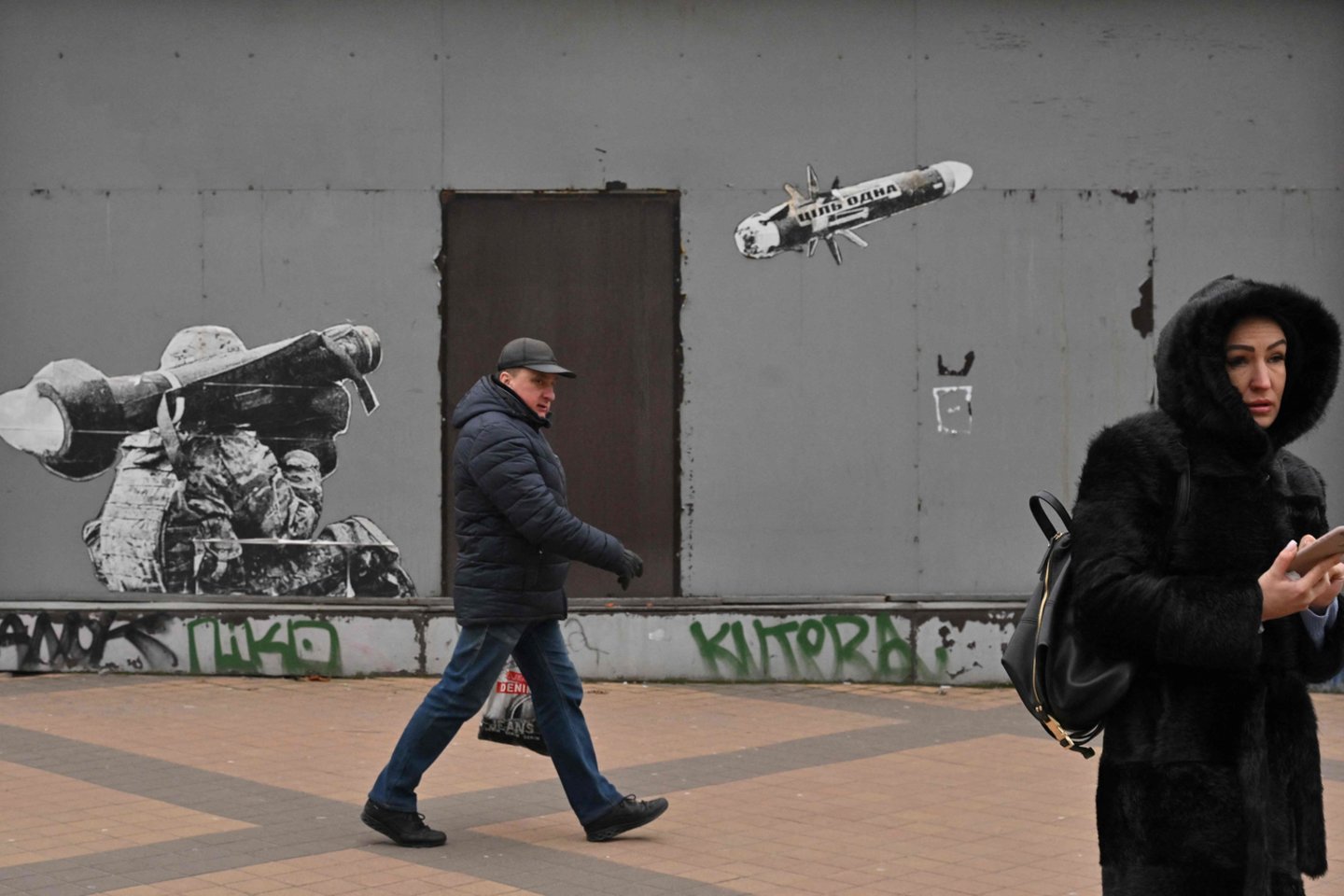  People walk past a graffiti on a wall depicting a Ukrainian soldier firing a portable anti-tank missile system, in Kyiv on January 25, 2023.<br> AFP / Scanpix nuotr.