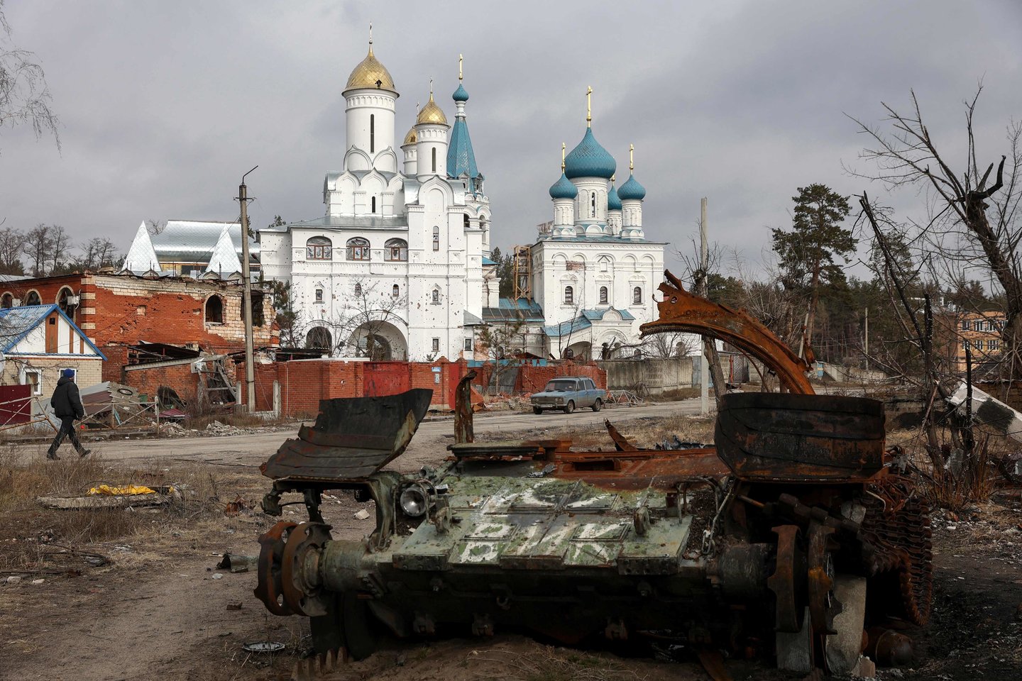  Vietos gyventojas 2023 m. kovo 1 d. eina pro apgadintą bažnyčią ir sunaikintą rusų tanką Sviatogirsko mieste Donecko srityje.<br> AFP / Scanpix nuotr.