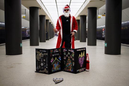 Kalėdų Senelio kostiumu persirengęs dailininkas, pasivadinęs „Ješešua“, gieda kalėdines giesmes metro stotyje Berlyne, Vokietijoje.<br>EPA-ELTA nuotr.