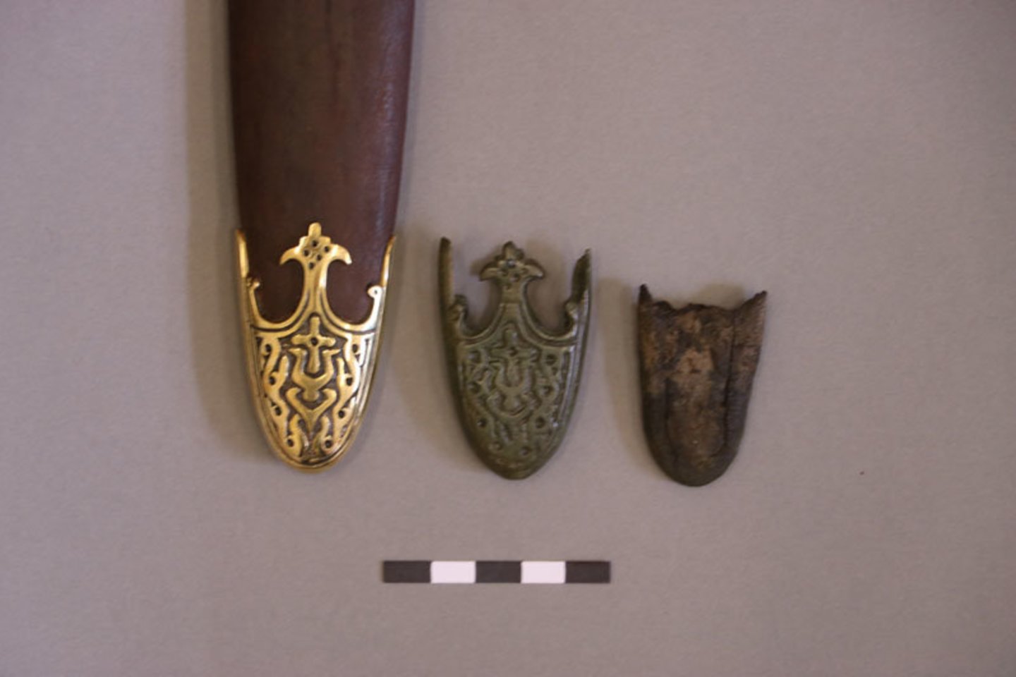 Medinių, oda aptrauktų ginklo makštų apkalas: pagamintas (išlietas) iš žalvario, iš abiejų pusių ornamentuotas paslaptingais motyvais.<br> D. Nikitenkos nuotr.