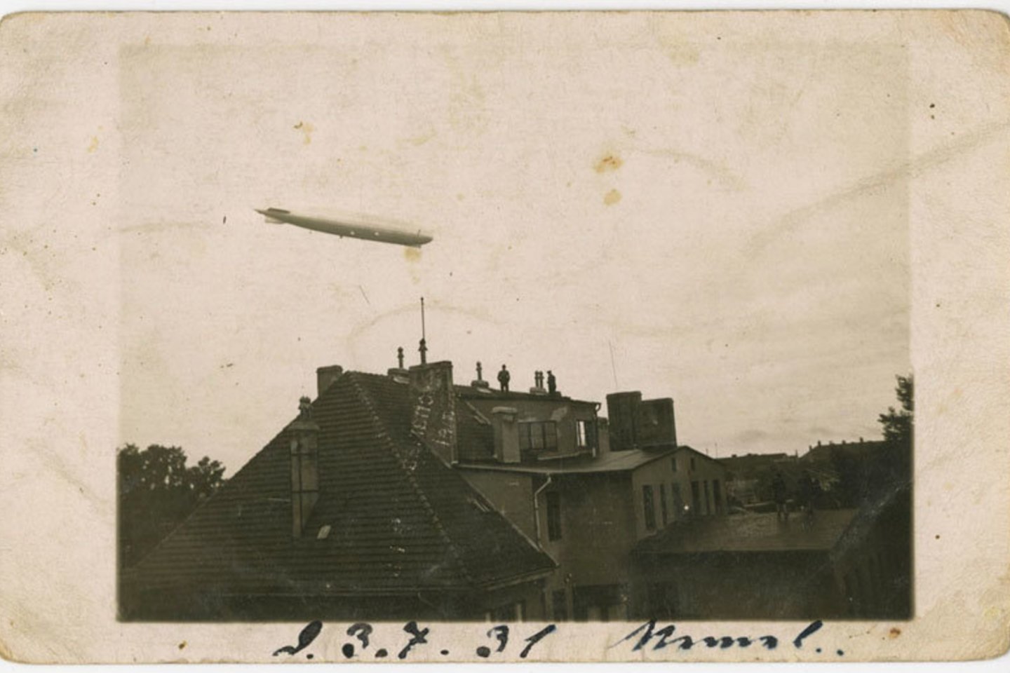 Virš Klaipėdos 1930-aisiais skrendantį orlaivį „Graf Zeppelin“ stebi ant stogų užlipę žmonės. Tai yra vienintelė žinoma autentiška, nesurežisuota to istorinio ryto fiksacija. <br> Lietuvos jūrų muziejaus nuotr.